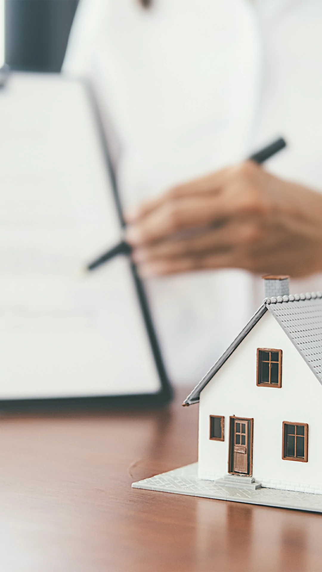 Modelo de casa sobre uma mesa com Contrato Promessa de Compra e Venda do projeto Compramos a sua casa hoje.
